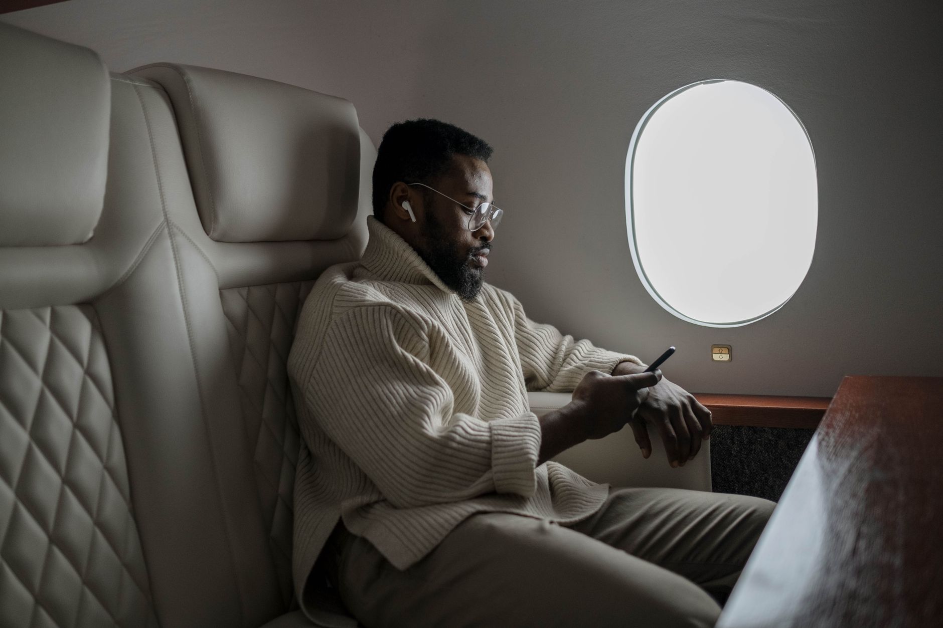 Bearded man in cozy sweater using smartphone on airplane, enjoying in-flight entertainment.